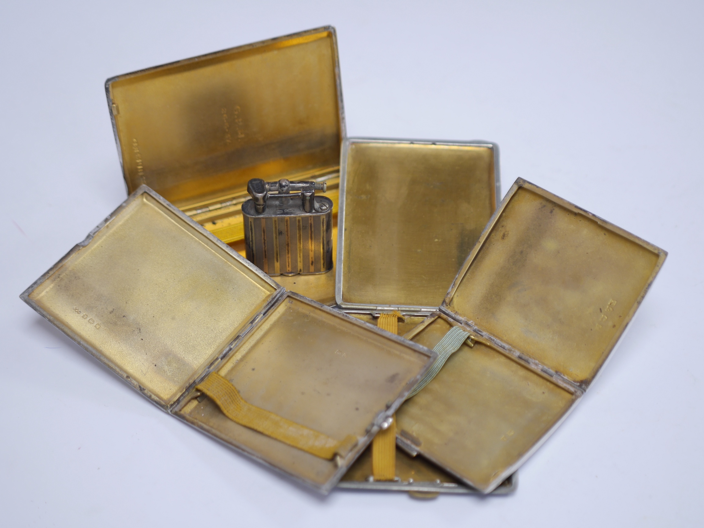 Three assorted George V silver and enamel cigarette cases, each decorated with a pennant, the largest by Benzies of Cowes, 11.6cm, one other French cigarette case and a 1920's silver lighter with import marks. Condition